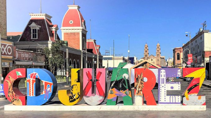 A vibrant "Cd. Juárez" sign stands proudly in downtown Ciudad Juárez, Chihuahua, symbolizing the city's rich cultural heritage and dynamic spirit. Behind the sign, the historic architecture of the city and the Cathedral of Our Lady of Guadalupe can be seen, showcasing the blend of modern and traditional influences in this bustling border city.