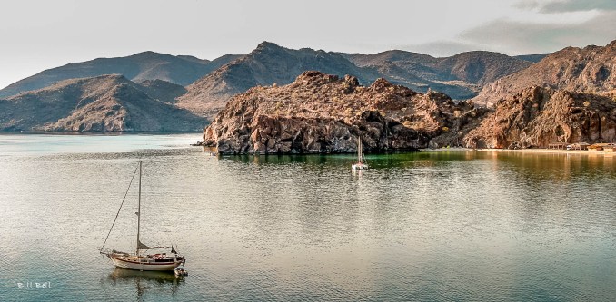 Sailboats gently float in the calm waters of Bahia Conception, framed by the picturesque rocky cliffs and tranquil scenery of the Baja California Peninsula.