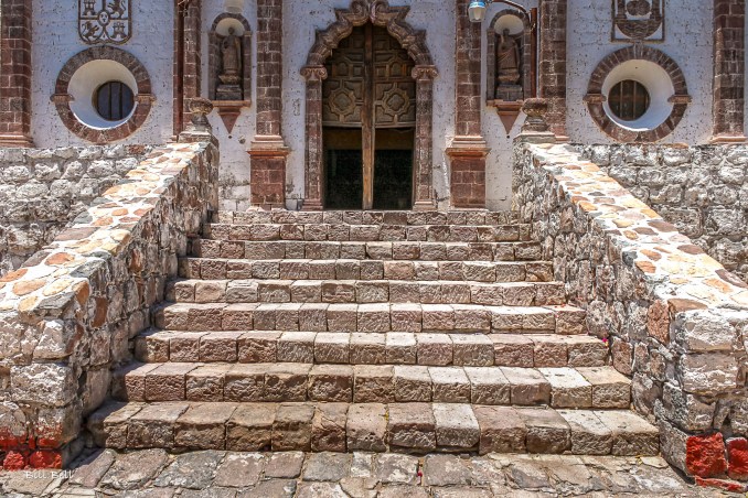 A closer view of the entrance steps leading to the Mission of San Ignacio, inviting visitors to explore its tranquil interiors. The stone steps and detailed wooden doorway capture the timeless character of this desert sanctuary.