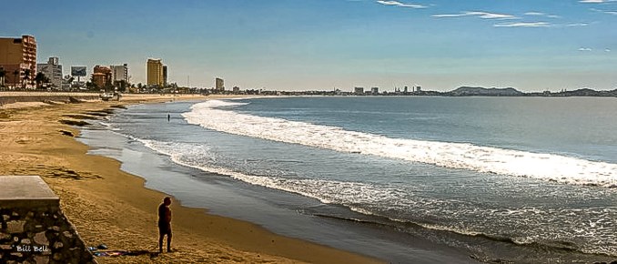 A lone figure enjoys the morning calm on Mazatlán's expansive beachfront, with the skyline of resort hotels stretching into the distance along the golden sands.