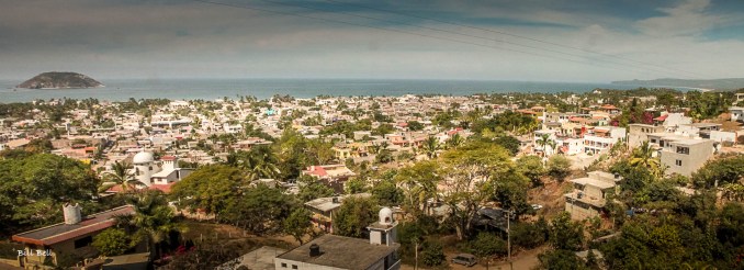 A panoramic view of La Peñita de Jaltemba, with its sprawling townscape leading out to the serene waters of the Pacific Ocean, framed by lush hills in the distance.