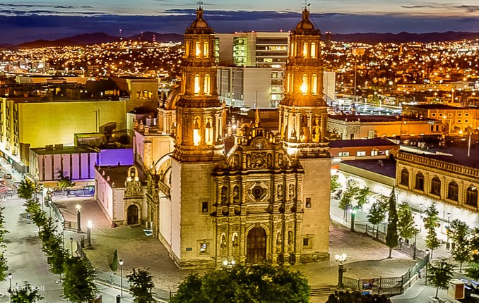 The Chihuahua Cathedral stands proudly illuminated against the vibrant backdrop of the city lights, showcasing its architectural splendor and historical significance.