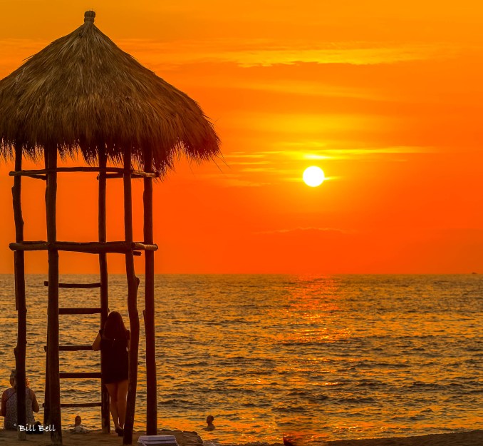 A breathtaking sunset over the Pacific Ocean in Puerto Vallarta, with a traditional palapa watchtower silhouetted against the golden sky. The city’s coastline offers some of the most stunning sunsets in all of Mexico.