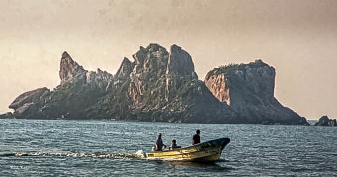 Local fishermen navigate their boat near the striking rock formations of Barra de Navidad, a testament to the town's enduring connection to the sea and its rich maritime heritage. ©Bill Bell