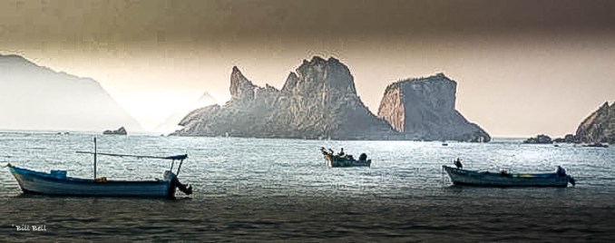 Fishing boats gently float in the calm waters of Barra de Navidad, with the dramatic rocky outcrops of Bahía de Navidad creating a stunning backdrop. This serene scene captures the essence of the town's peaceful coastal life. ©Bill Bell