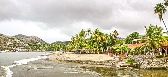 The serene beachside view of Zihuatanejo, where the calm waters meet the lush greenery, offering a peaceful retreat for those seeking relaxation.