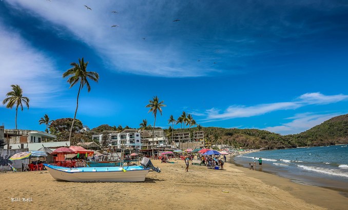 A view of the bustling Los Ayala beach with food stalls, umbrellas, and tourists enjoying the sun and sand.