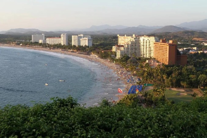 A panoramic view of Ixtapa's bustling beachfront, lined with luxury resorts and framed by the lush mountains of Guerrero. Visitors enjoy the golden sand and calm waters of the Pacific Ocean, making Ixtapa a perfect destination for relaxation and adventure.