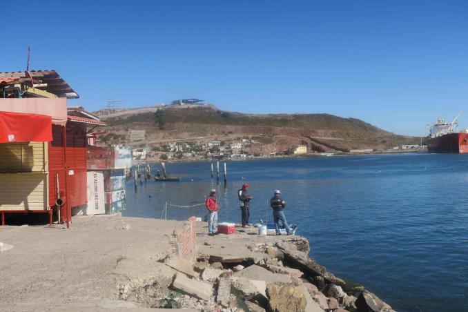 Fishermen enjoy a quiet morning on the docks at Topolobampo, Sinaloa. The area is a popular spot for fishing, with views of the town and industrial ports in the distance."