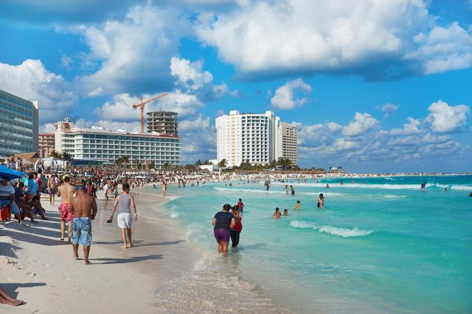 Tourists enjoy the sun and surf along the bustling beachfront of Cancún's Zona Hotelera. This vibrant area is known for its beautiful white sand beaches, turquoise waters, and high-rise hotels, offering a perfect mix of relaxation and excitement against a backdrop of striking coastal scenery.