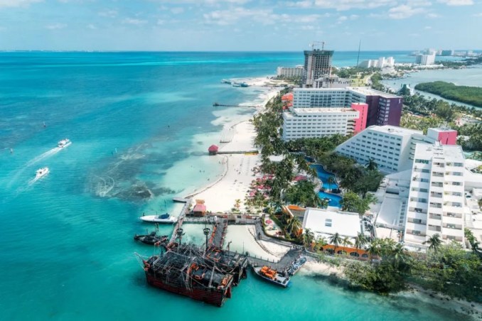 A stunning aerial view of Cancún's Zona Hotelera, showcasing its pristine white sand beaches, turquoise Caribbean waters, and high-rise hotels. This vibrant area is the heart of Cancún's tourism, offering luxurious resorts, lively nightlife, and endless entertainment options for visitors.