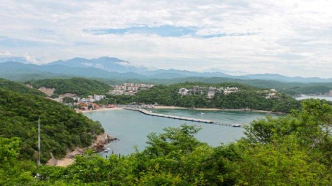 Overlooking Huatulco’s harbor, with its calm waters and vibrant greenery, set against the backdrop of distant mountains.