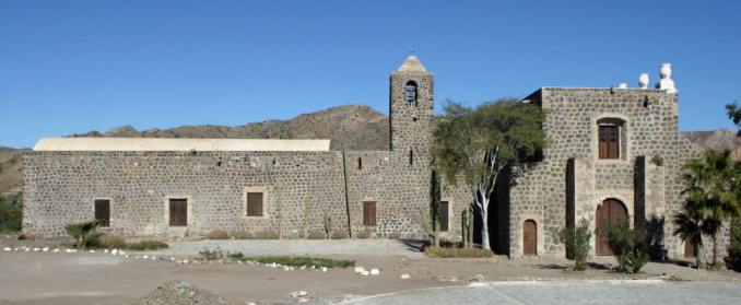 The full view of Mission Santa Rosalía de Mulegé, showcasing its distinctive stone construction and serene surroundings in the Mulegé valley.