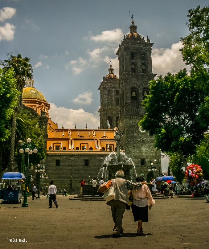 An elderly couple enjoys a leisurely walk in Puebla's Zócalo, the city's central square, where the grand cathedral stands as a testament to the city’s rich history.