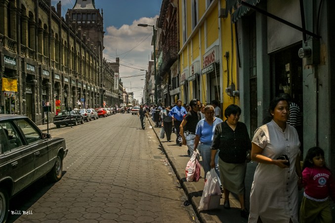  bustling street in Puebla City, where the historic architecture blends with the daily rhythm of life. Pedestrians navigate the narrow sidewalks under the watchful gaze of centuries-old buildings.